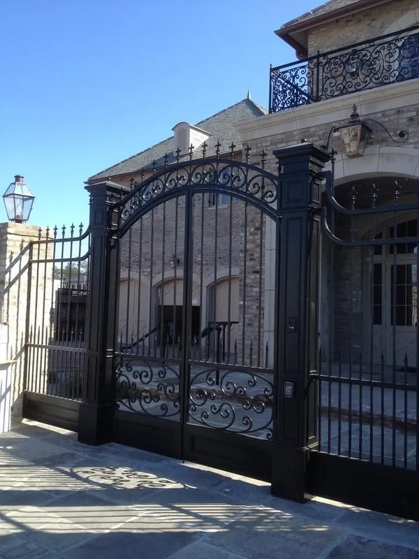 An arched iron gate with scrollwork in front of a house.