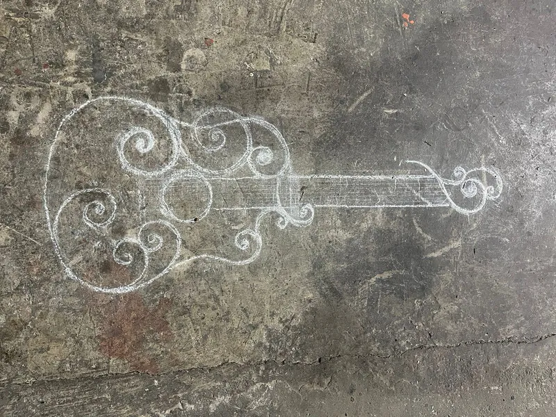 The outline of a guitar with scrolls, drawn in chalk on the workshop floor.